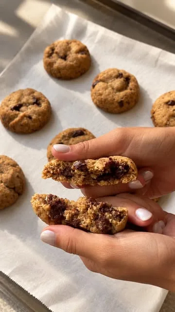 Mãos a partir uma cookie de pepitas de chocolate sobre um tabuleiro de cookies acabadas de sair do forno