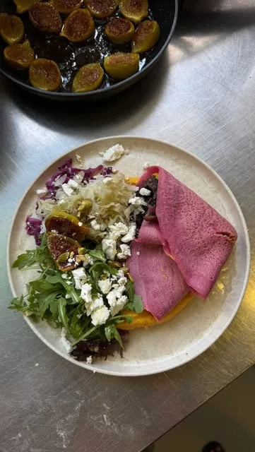 Prato com wrap cor-de-rosa, rúcula, feta, couve roxa e figos caramelizados, com uma frigideira de figos ao fundo